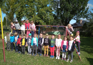 Dzieci w ogrodzie przedszkolnym. Część weszła na drabinki, pozostali stoją opierając się o nie.